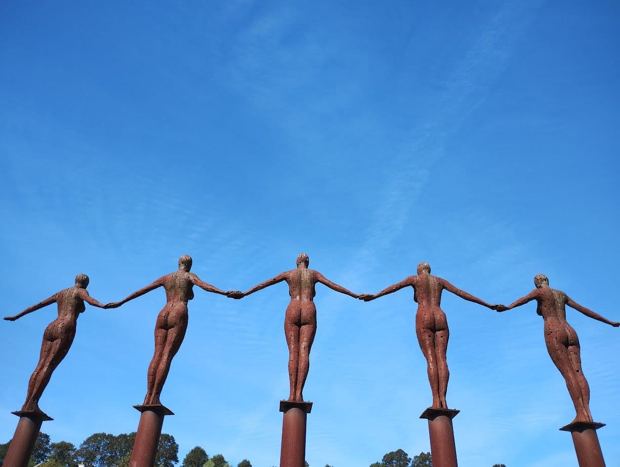 Five sculpted figures holding hands against the sky